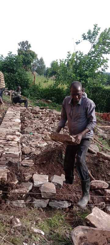 A builder lays bricks beside a pile of stones on the building site