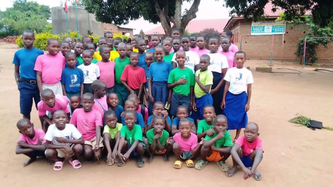A large group of children in bright T-shirts and school uniforms stand together in the school yard