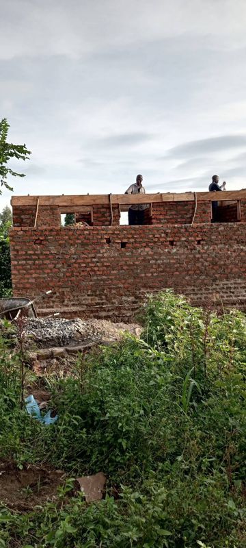 The brick walls of the new dormitory rise behind green bushes