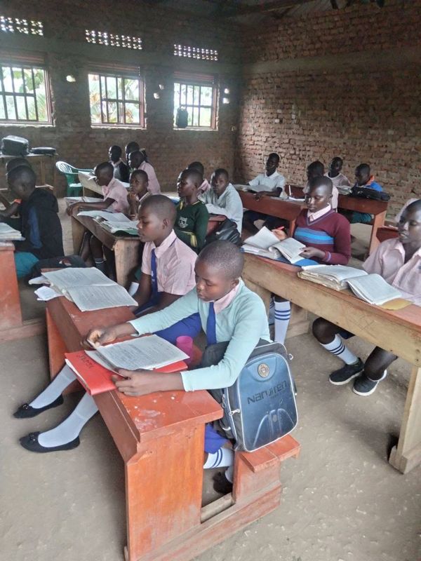 Pupils in pink and blue uniforms write in their exercise books at wooden desks